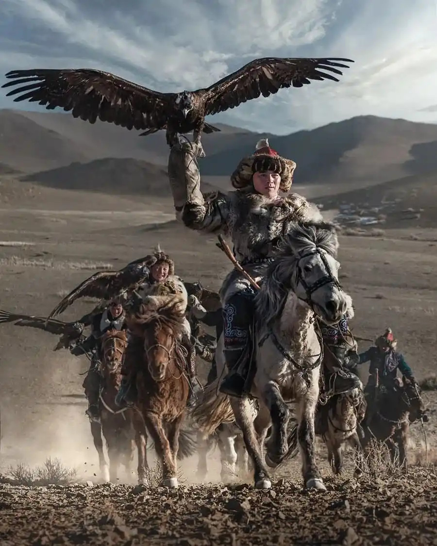 A Kazakh eagle hunter in traditional dress holding a golden eagle while riding a horse in the Altai Mountains, Mongolia.