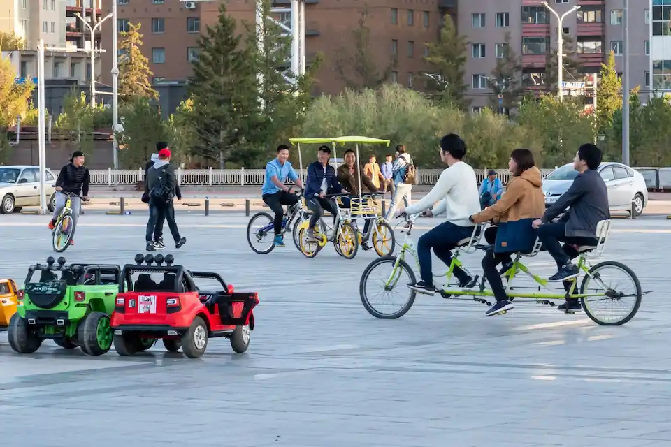 Tourists enjoying a peaceful day in a Mongolian public square with bikes and toy cars, highlighting safe and family-friendly travel.