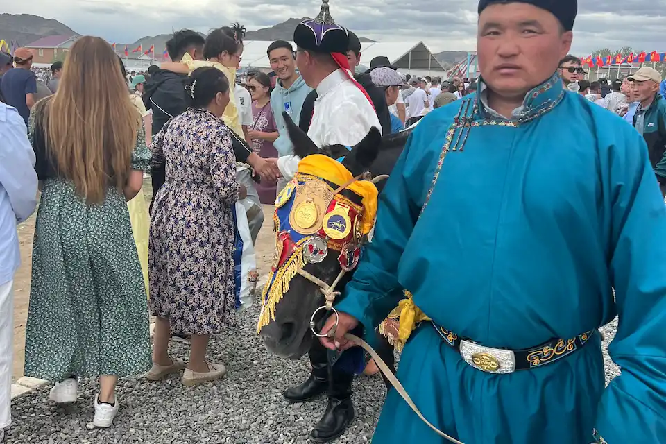 A proud moment at Naadam — traditional attire, decorated horse, and community celebration in Altai Tavan Bogd