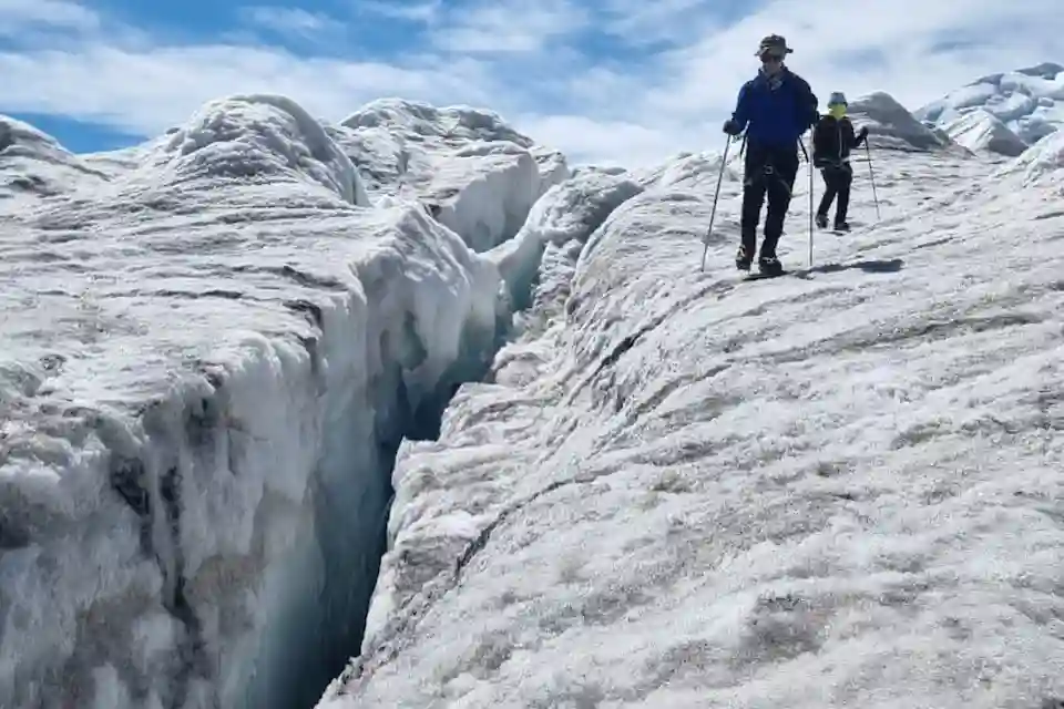 Glacier hikers carefully traverse a narrow icy path beside a dramatic crevasse in Altai Tavan Bogd