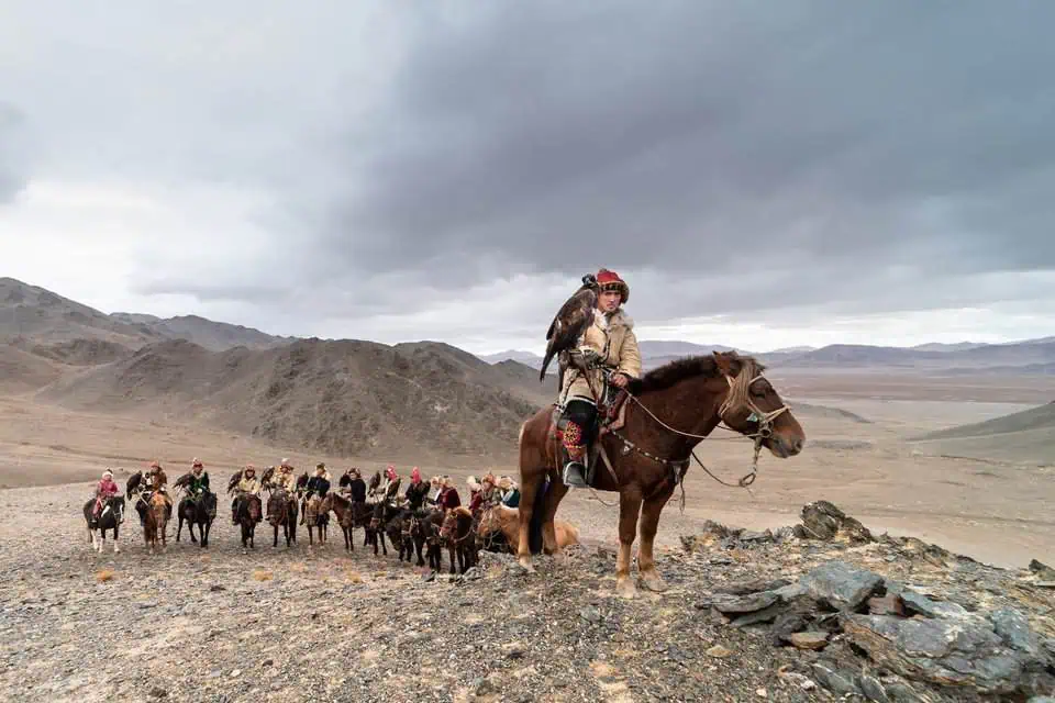 A Kazakh eagle hunter rides through the rugged Altai terrain at dusk, his golden eagle poised for flight. This dramatic moment captures the harmony between tradition and wilderness.